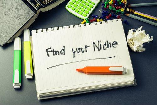 A Notepad with find your niche written on it in black pen with multi-coloured pens around it