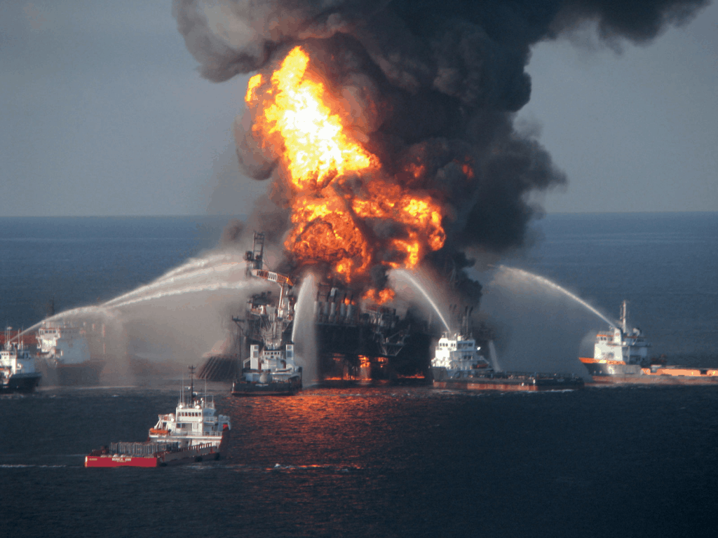 Image of BP Oil's Deepwater Horizon spill with a rig on fire at sea and shits spraying water onto the fire and black smoke